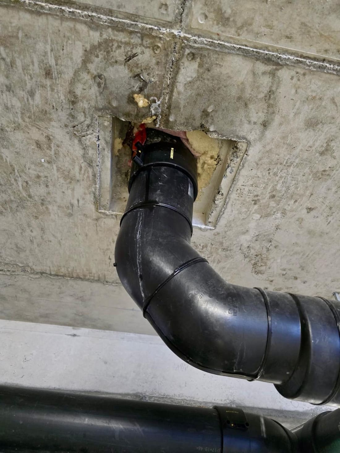 Conduite d’évacuation noire traversant une dalle en béton, réservation ouverte autour