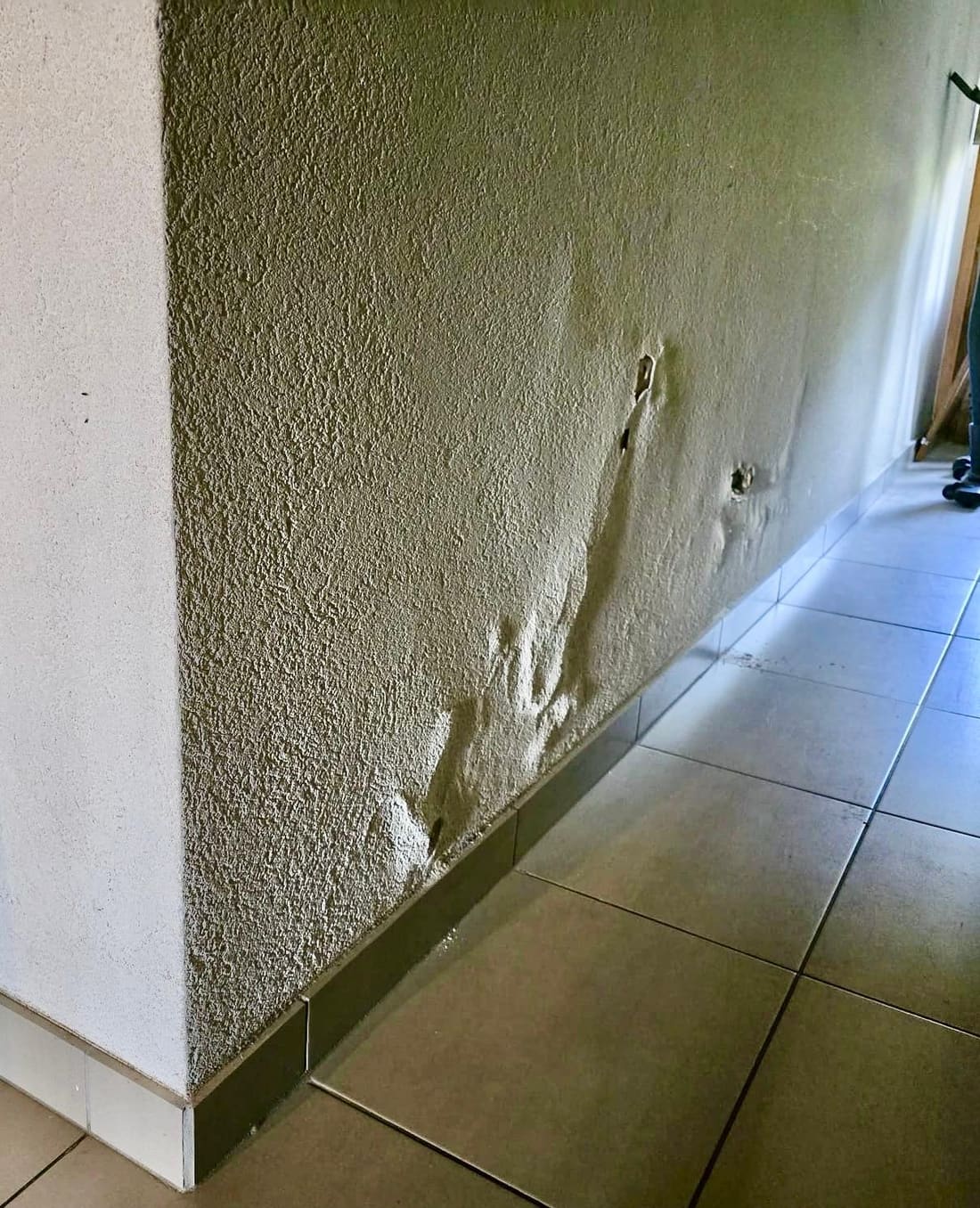 Crépi gonflé et décollé en pied de mur, au-dessus de la plinthe